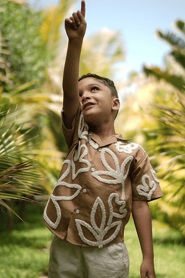 A child pointing at something in the sky while wearing a brown cotton shirt with unique 3D hand embroidery in a floral pattern.