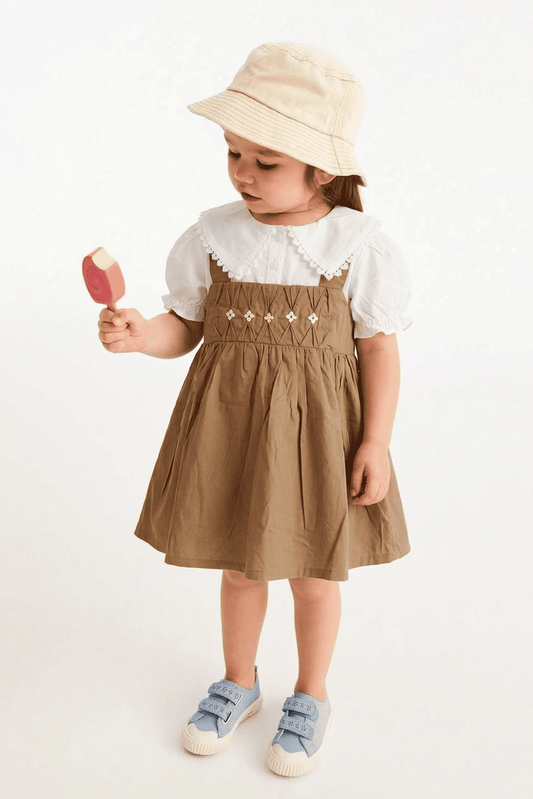 Child wearing a brown dress with white lace details, holding a pink toy, on a white background