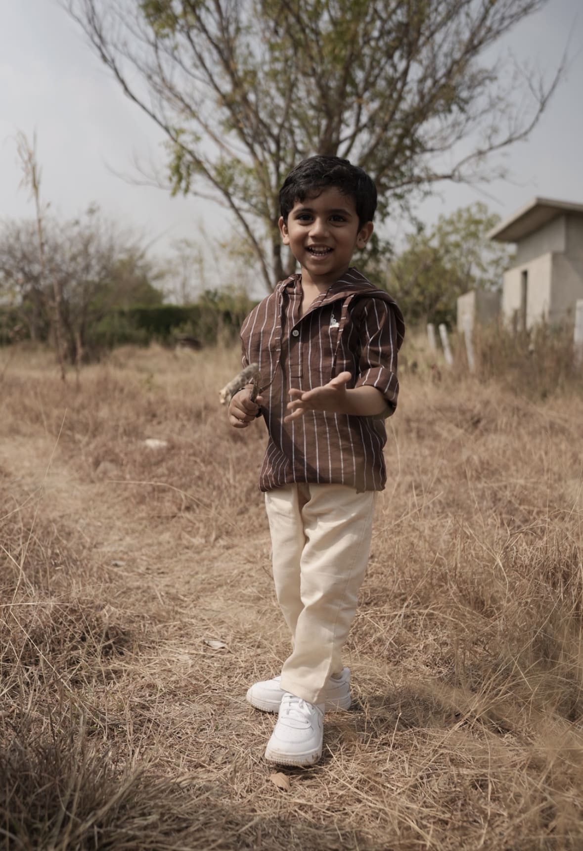Child standing in a dry field with trees and a house in the background