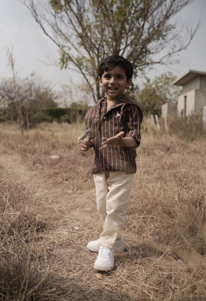 Child standing in a dry field with trees and a house in the background