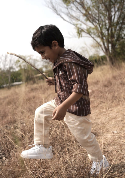 Child in a striped shirt and beige pants standing in a field with a stick
