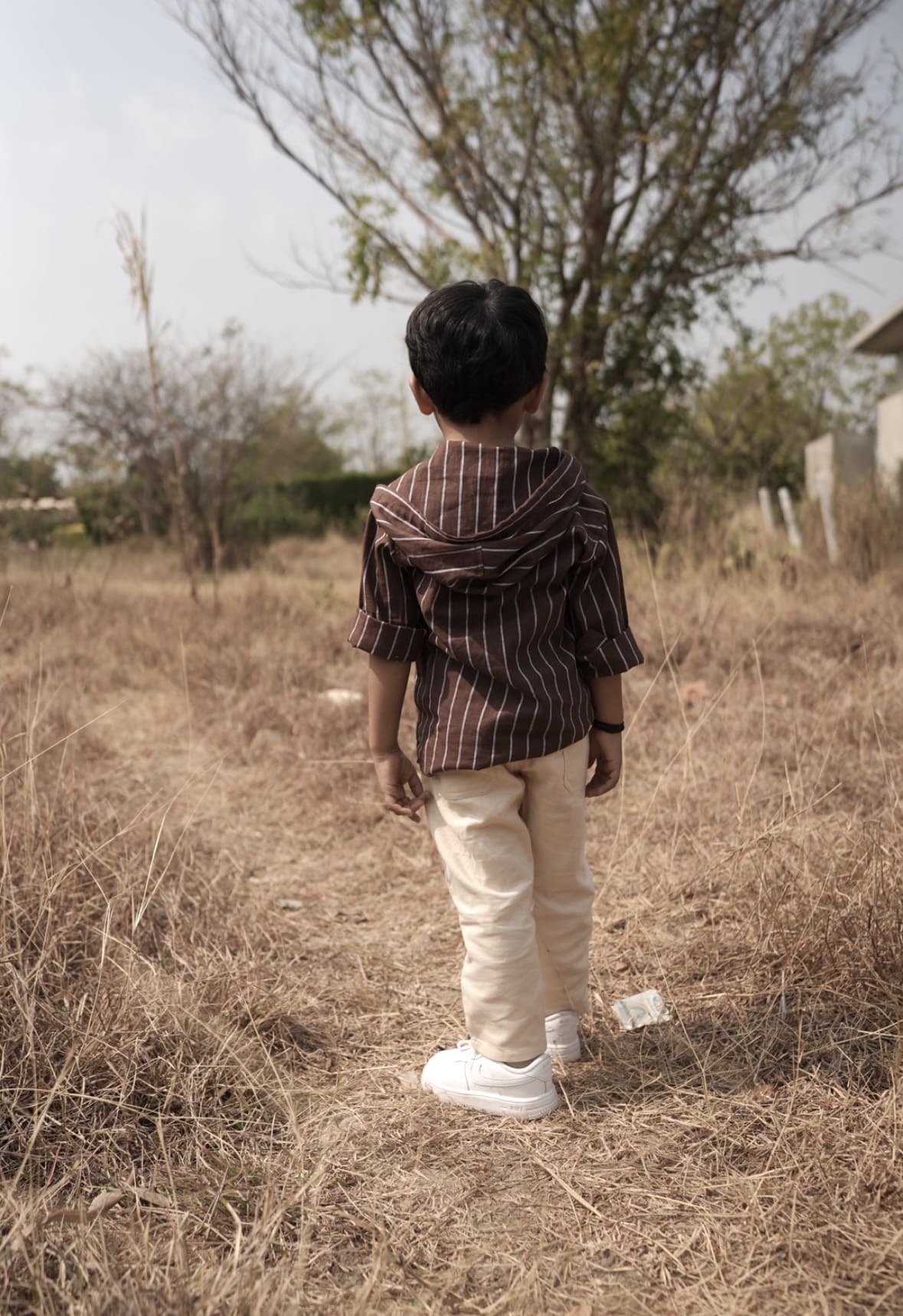 Child standing in a dry field with trees in the background