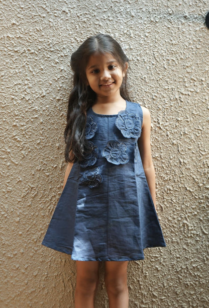 Young girl wearing a blue floral dress against a textured wall.
