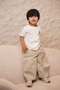 Child in a white shirt and beige pants standing on a sandy surface