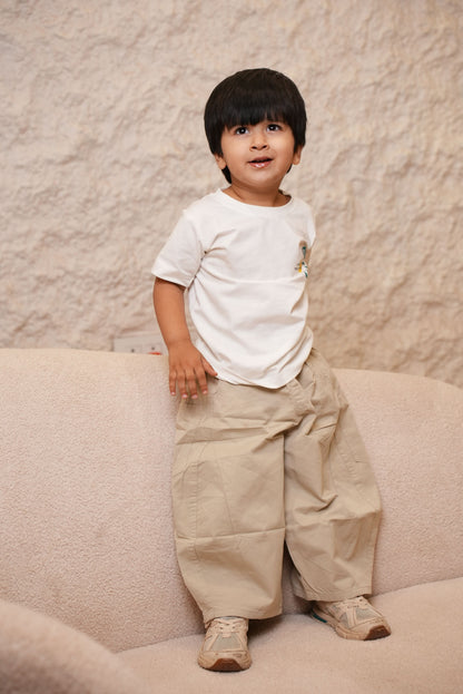 Child in a white shirt and beige pants standing on a sandy surface