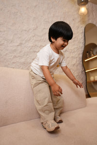 Child in a white shirt and beige pants standing on a light-colored floor.