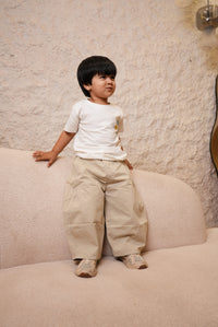 Child standing on a textured floor wearing a white shirt and beige pants.