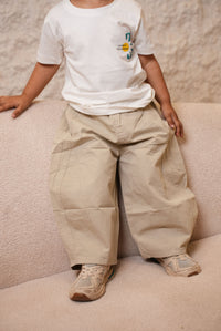 Person wearing beige pants and a white shirt with a logo on a light-colored carpet