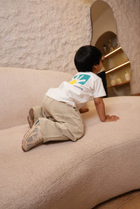 Child playing on a textured beige floor with a white shirt and brown shoes.