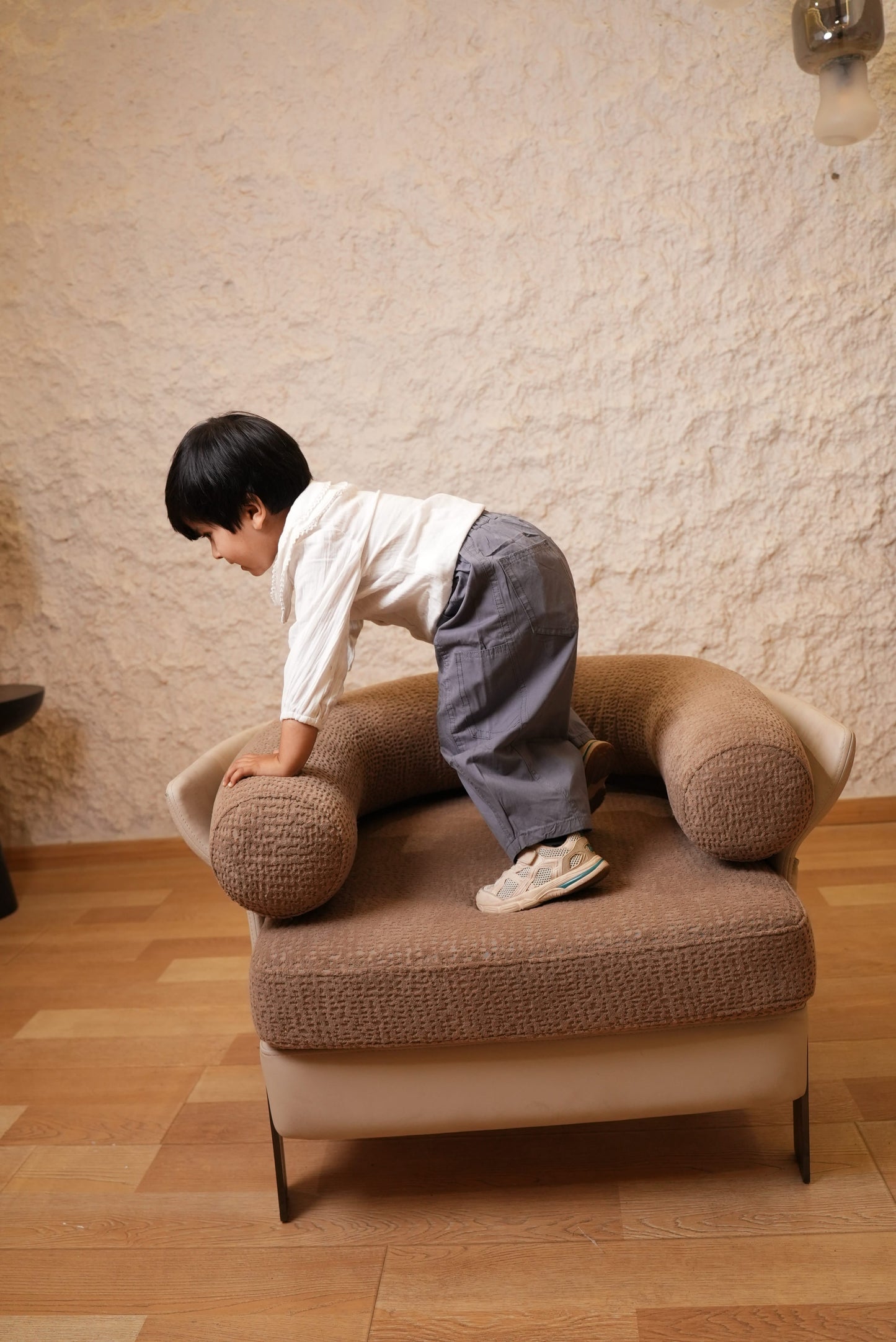 Child sitting on a brown chair in a room with wooden floor and beige walls.