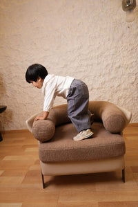 Child sitting on a brown chair in a room with wooden floor and beige walls.