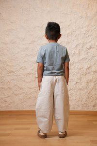 Person wearing a blue shirt and beige pants standing on a wooden floor with a textured wall background