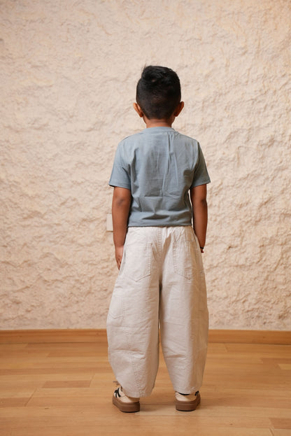 Person wearing a blue shirt and beige pants standing on a wooden floor with a textured wall background