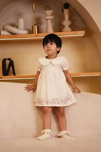 Child in a white dress standing in front of a mirror in a bathroom.