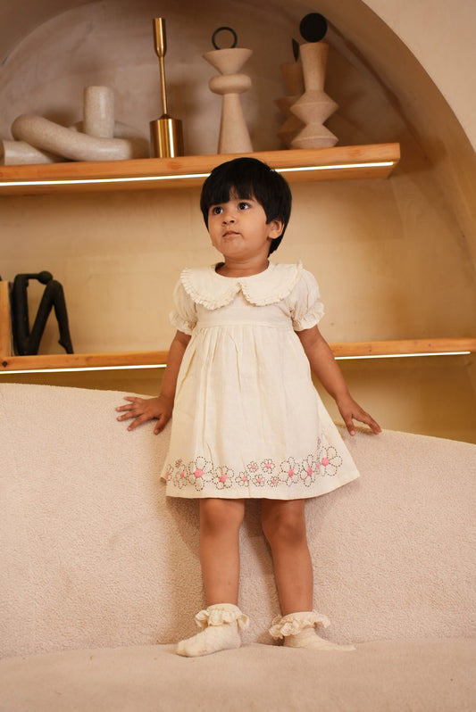 Child in a white dress standing in front of a mirror in a bathroom.