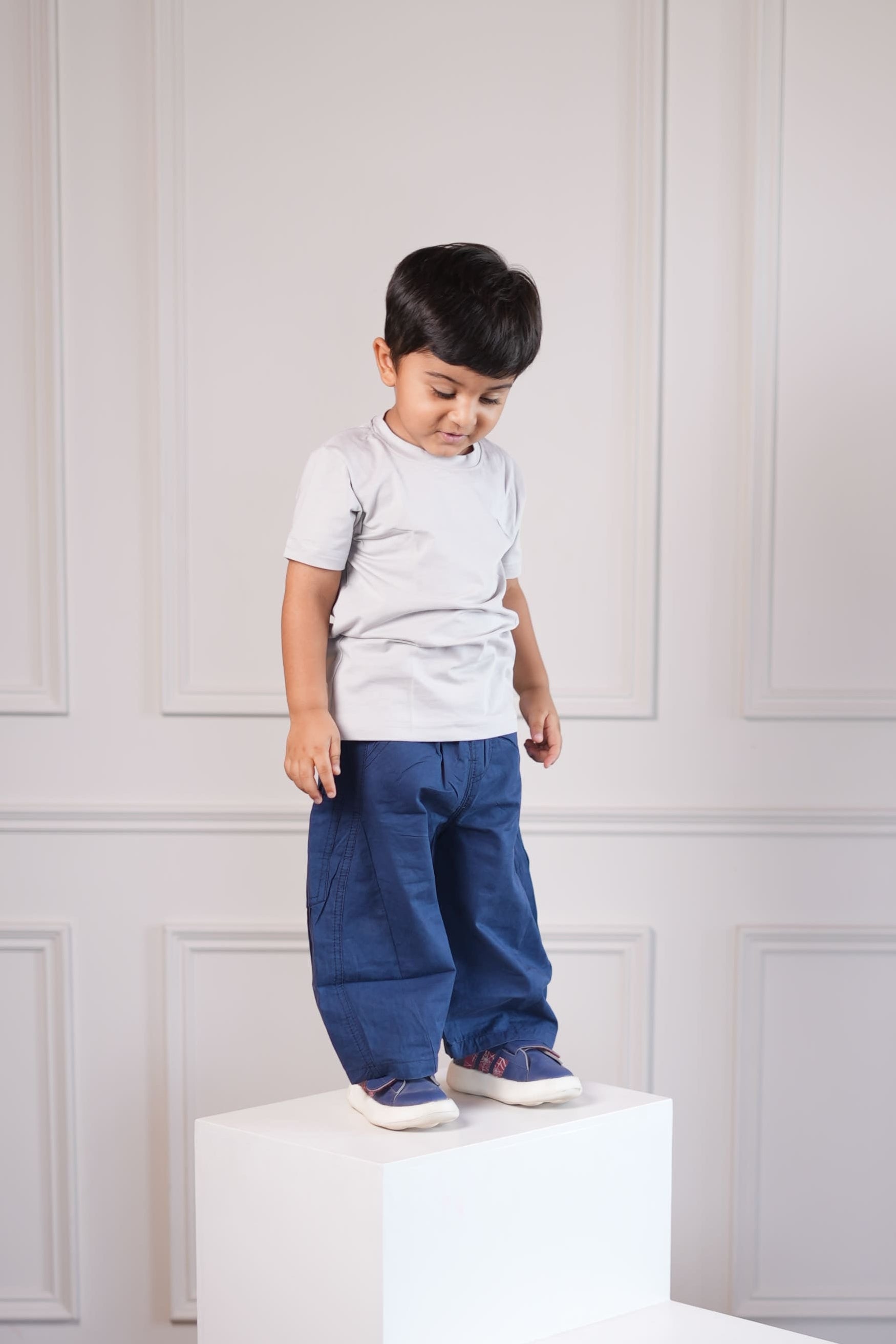 Child standing in a room with white furniture and wooden floor.