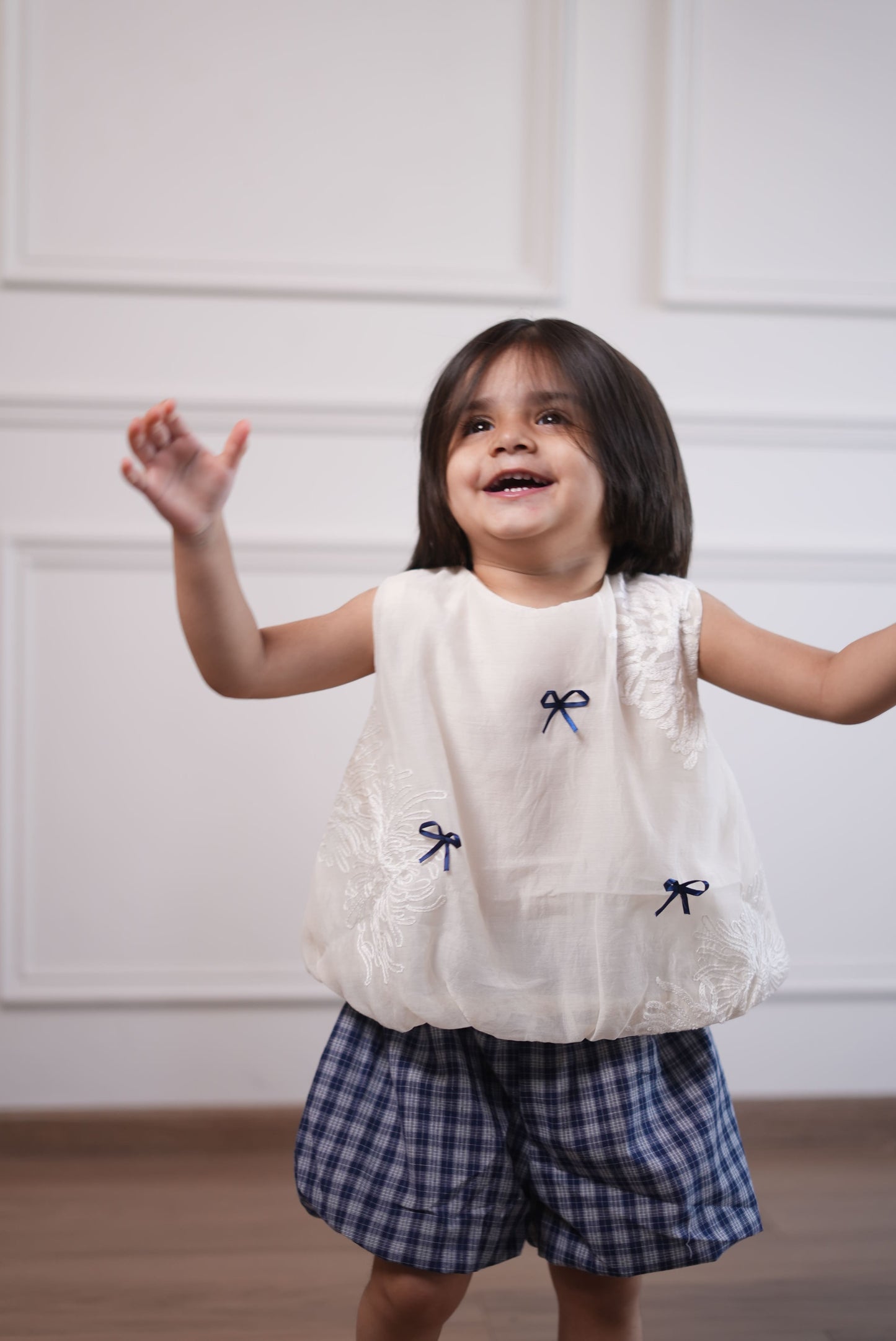 Child wearing a white dress with blue accents against a plain background