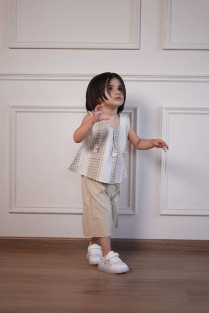 Child in a checkered dress standing against a white paneled wall.