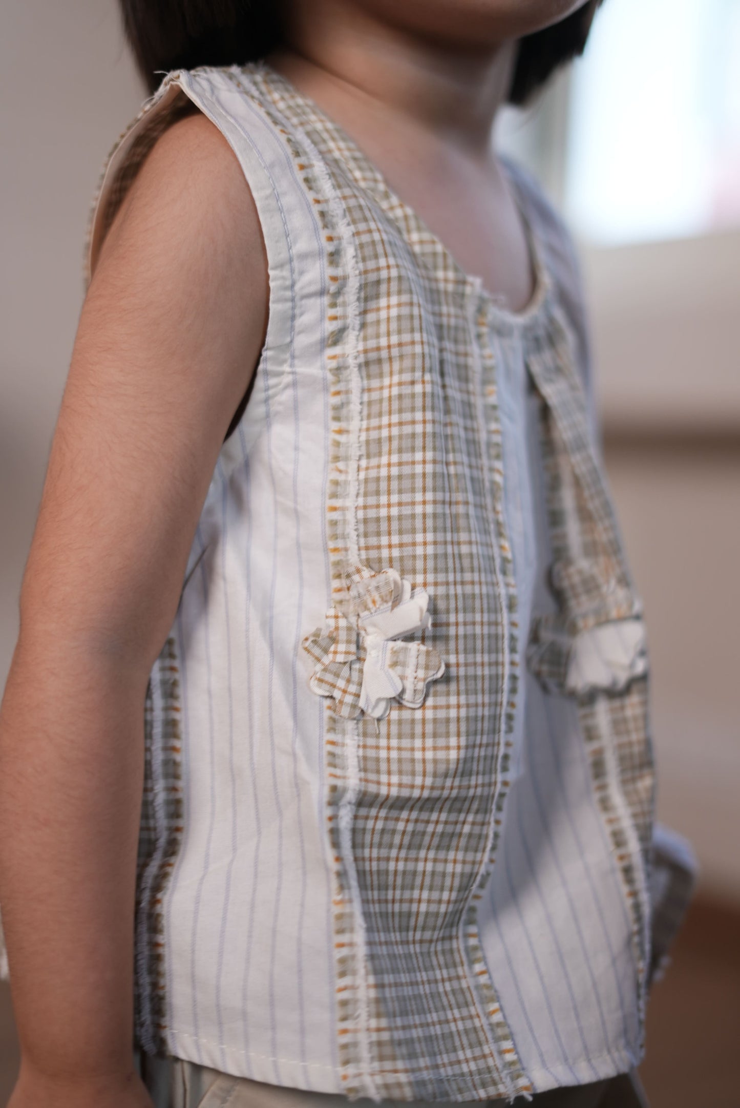 Person wearing a light-colored outfit with a checkered pattern, standing against a white wall.