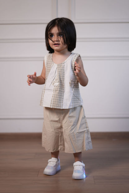 Person wearing a light-colored outfit with a checkered pattern, standing against a white wall.