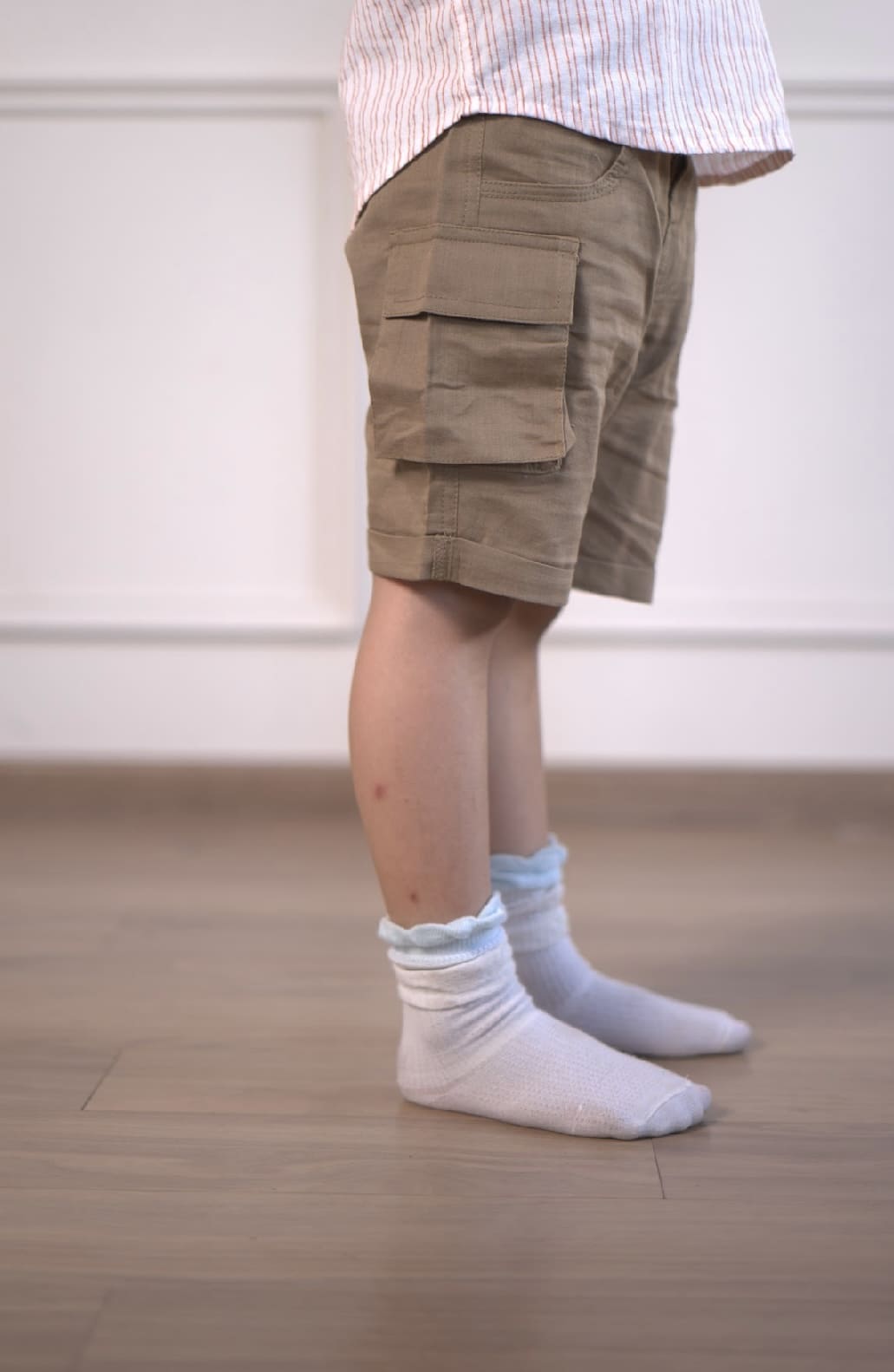 Person wearing beige cargo shorts and white socks on a wooden floor.
