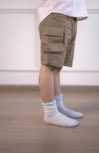 Person wearing beige cargo shorts and white socks on a wooden floor.