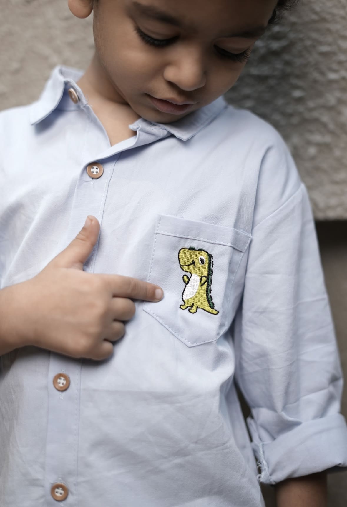 Child wearing a light blue shirt with a small patch on the chest.