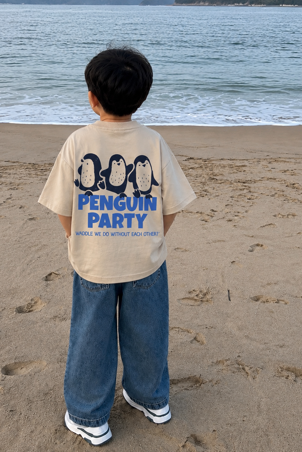 Child wearing a t-shirt with 'Penguin Party' design on a beach