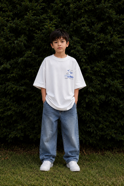 Child wearing a white t-shirt and blue jeans standing in front of dark green bushes.