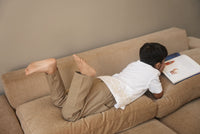 Person lying on a beige couch with a book open on their chest.