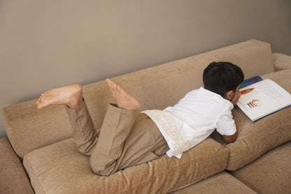 Person lying on a beige couch with a book open on their chest.