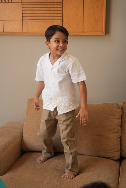 Child in a white shirt and beige pants standing on a brown couch.