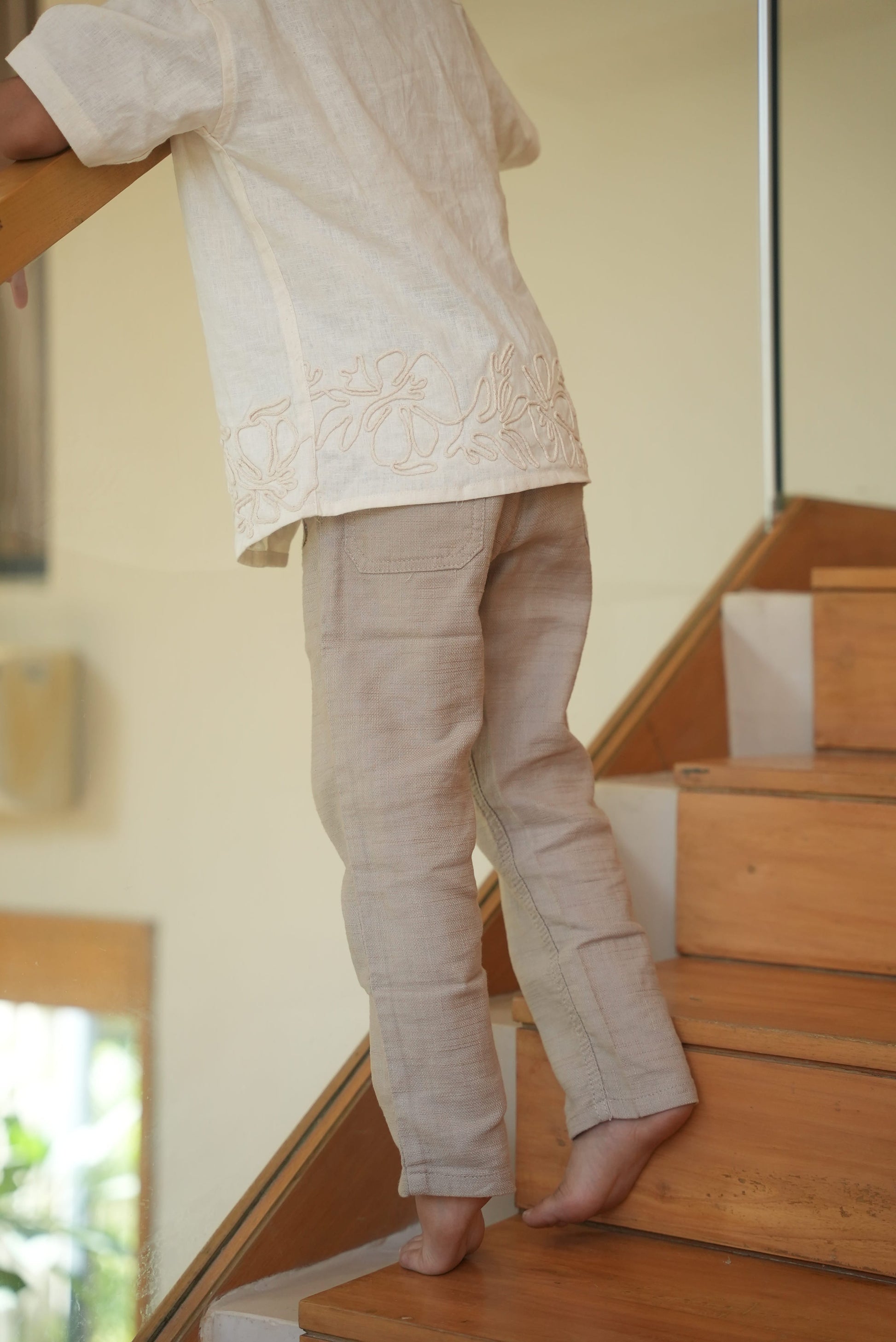 Person wearing beige pants and a white shirt sitting on a wooden staircase.