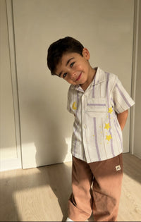 Child wearing a striped shirt with star designs and brown pants indoors.