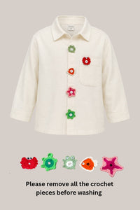 An off-white long-sleeve children's button-up shirt with colorful crocheted flower and starfish embellishments on the front and pocket. The image includes a text overlay at the bottom instructing to remove all crochet pieces before washing, with five small cropped views of the crochet pieces shown below the main shirt.