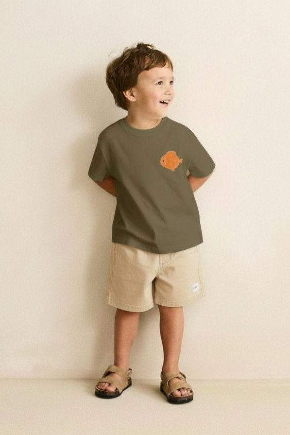 Child wearing a green t-shirt with a logo and beige shorts against a plain background