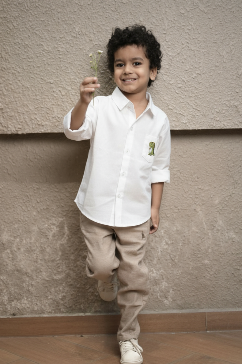 Child wearing a white shirt and beige pants against a plain wall.