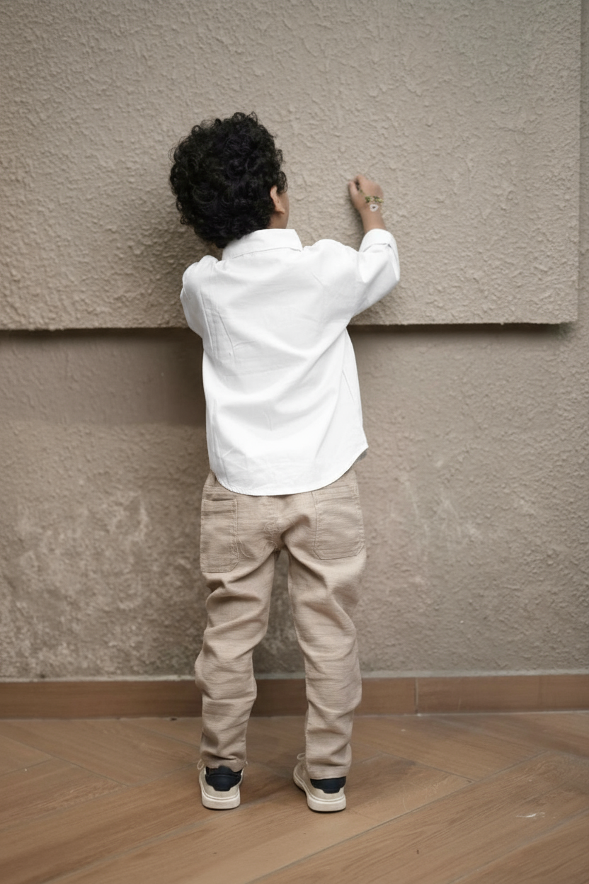 Person in a white shirt and beige pants standing against a textured wall.